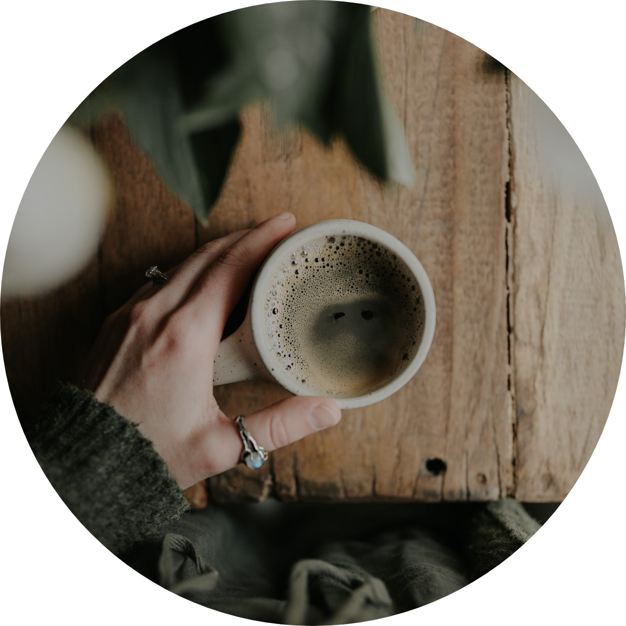 woman's hand with opal thumb ring touching a cup of hot tea on a wooden table