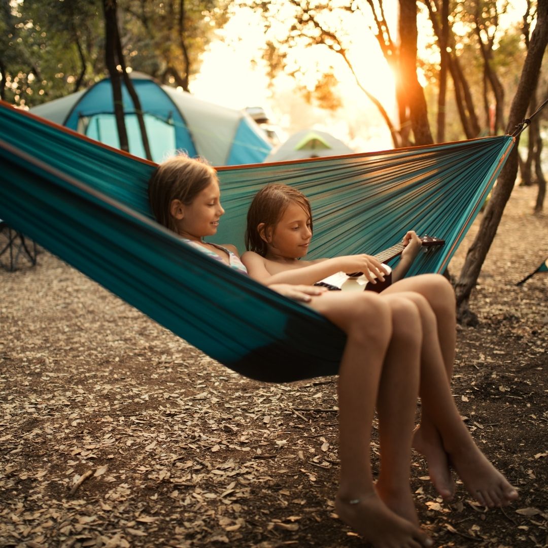 two girls sit in hammock and play ukulele
