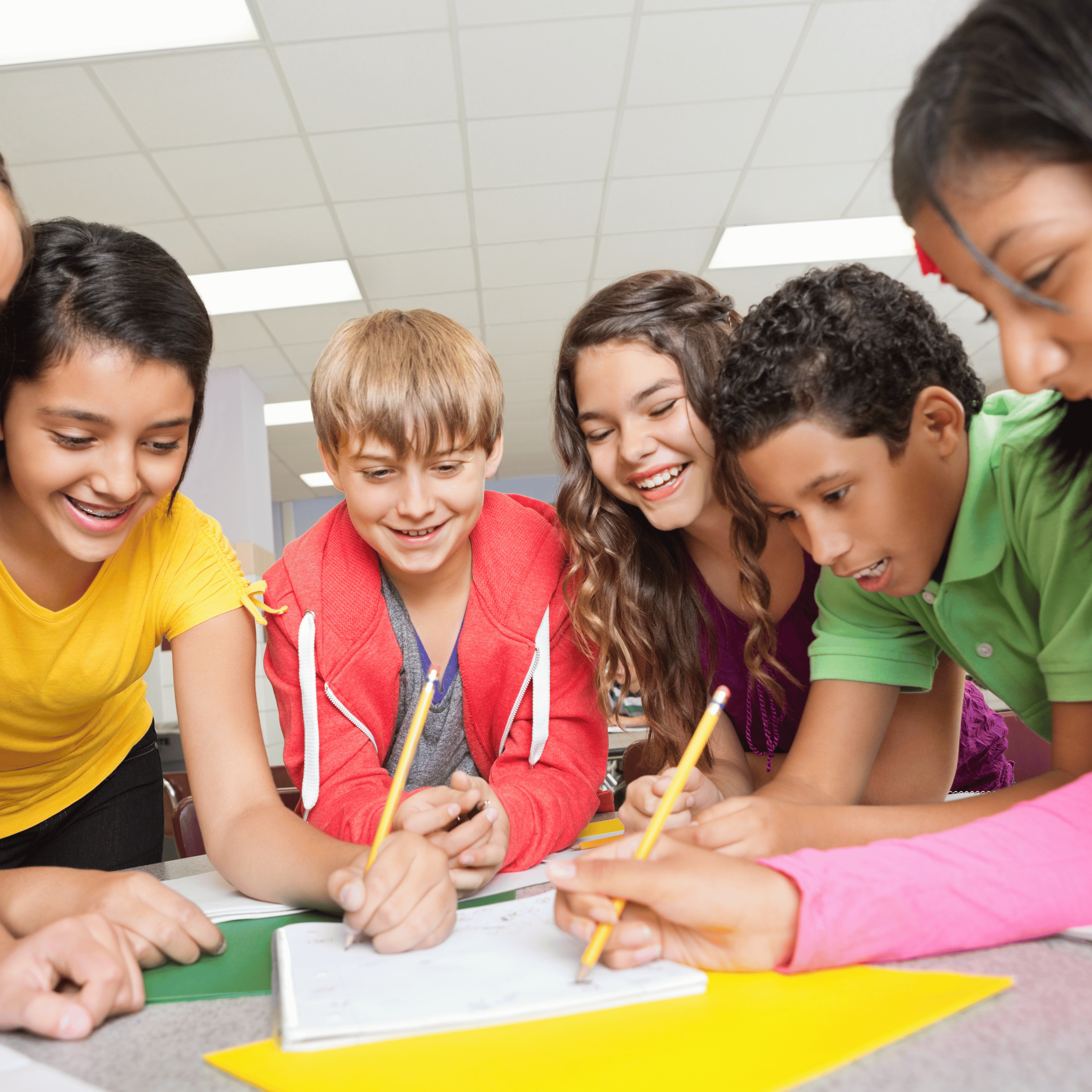 students leaning over classroom table using pencils