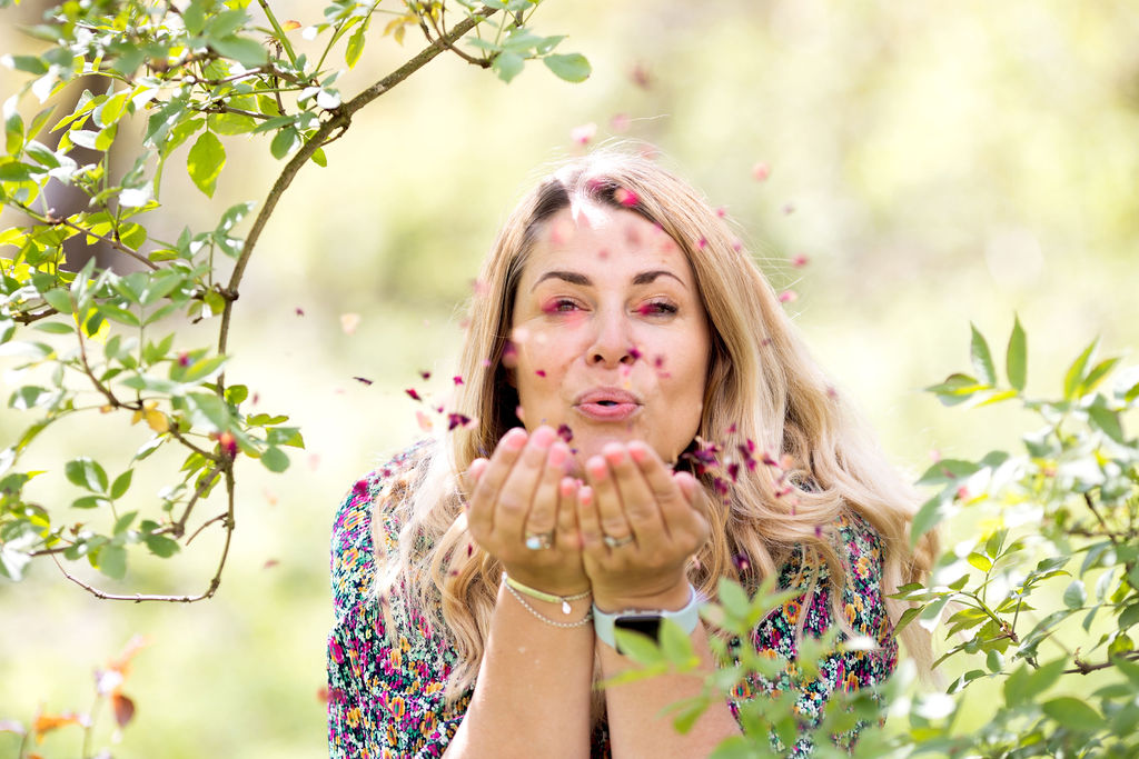 Emma from Los Social blowing petal confetti from behind some trees in the woods