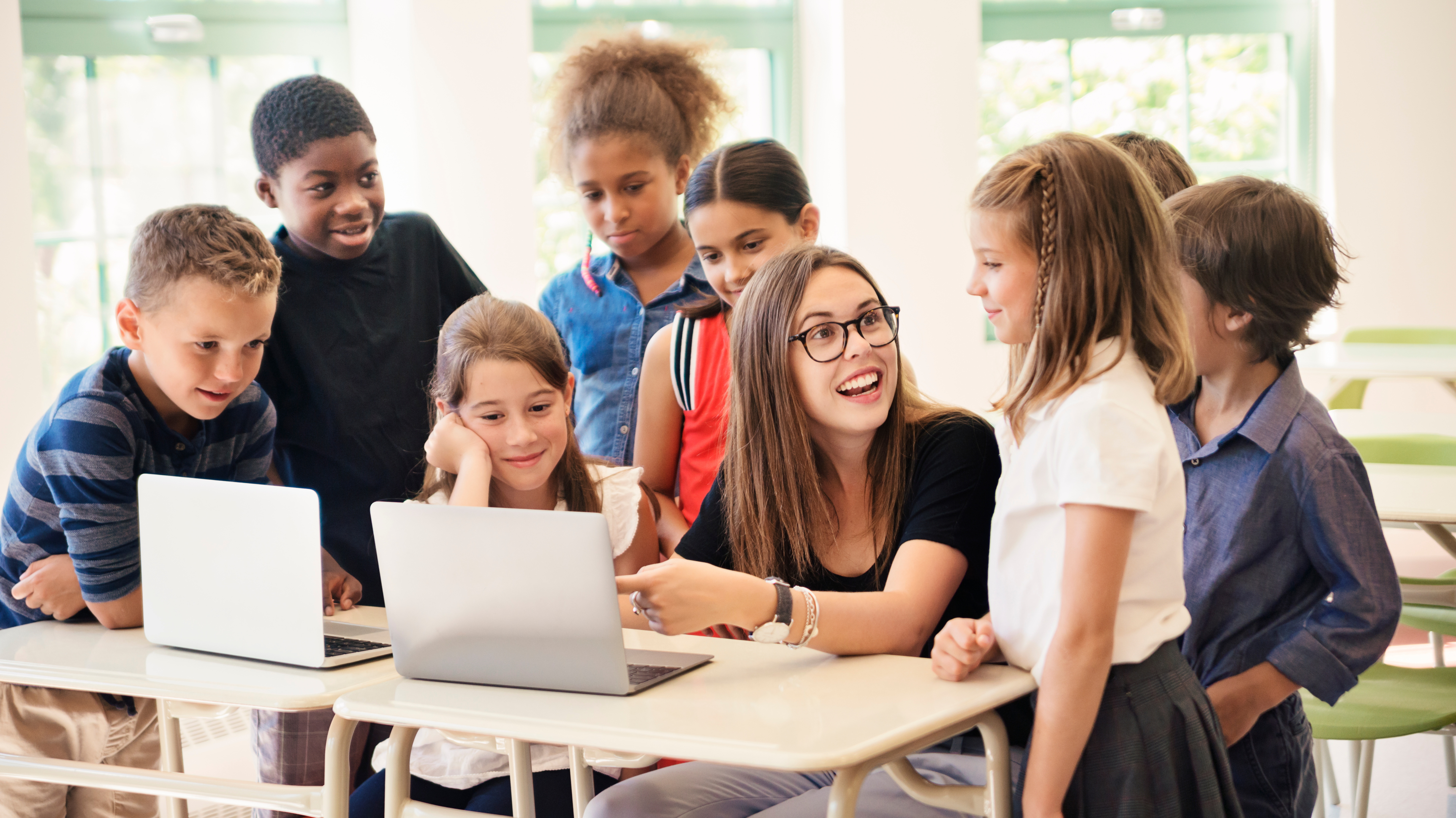 teacher sitting in front of laptops with students surrounding her