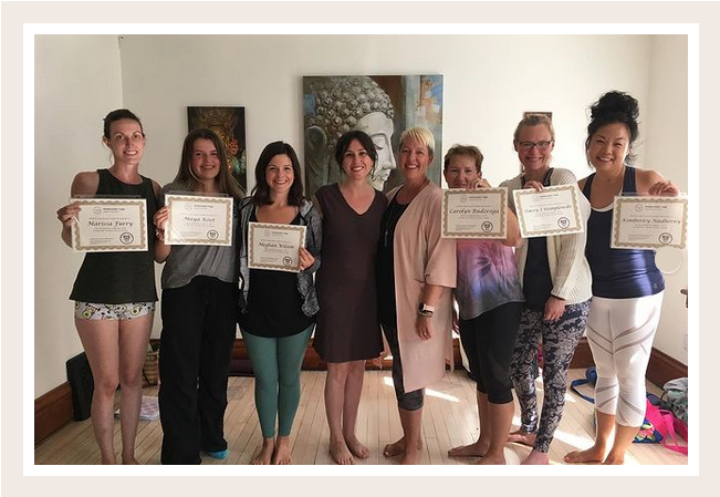 A group of smiling women stand in a line.  6 are holding yoga teacher certificates, 2 in the middle are their trainers smiling proudly. 