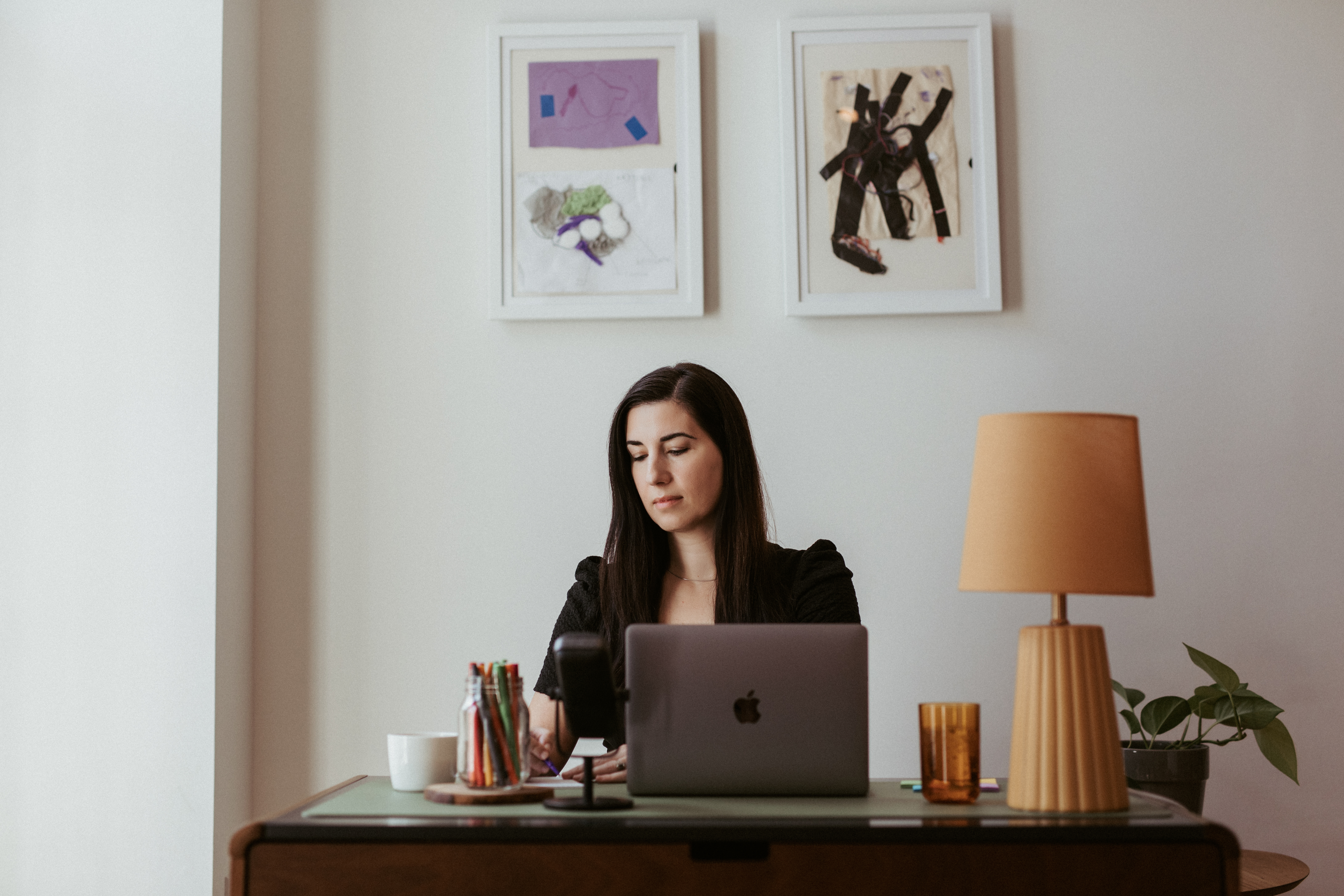 Birds eye view of a wood desk with a macbook, a green glass filled with water, a white mug filled with coffee and a textured dark green water cup with a lid and a straw.