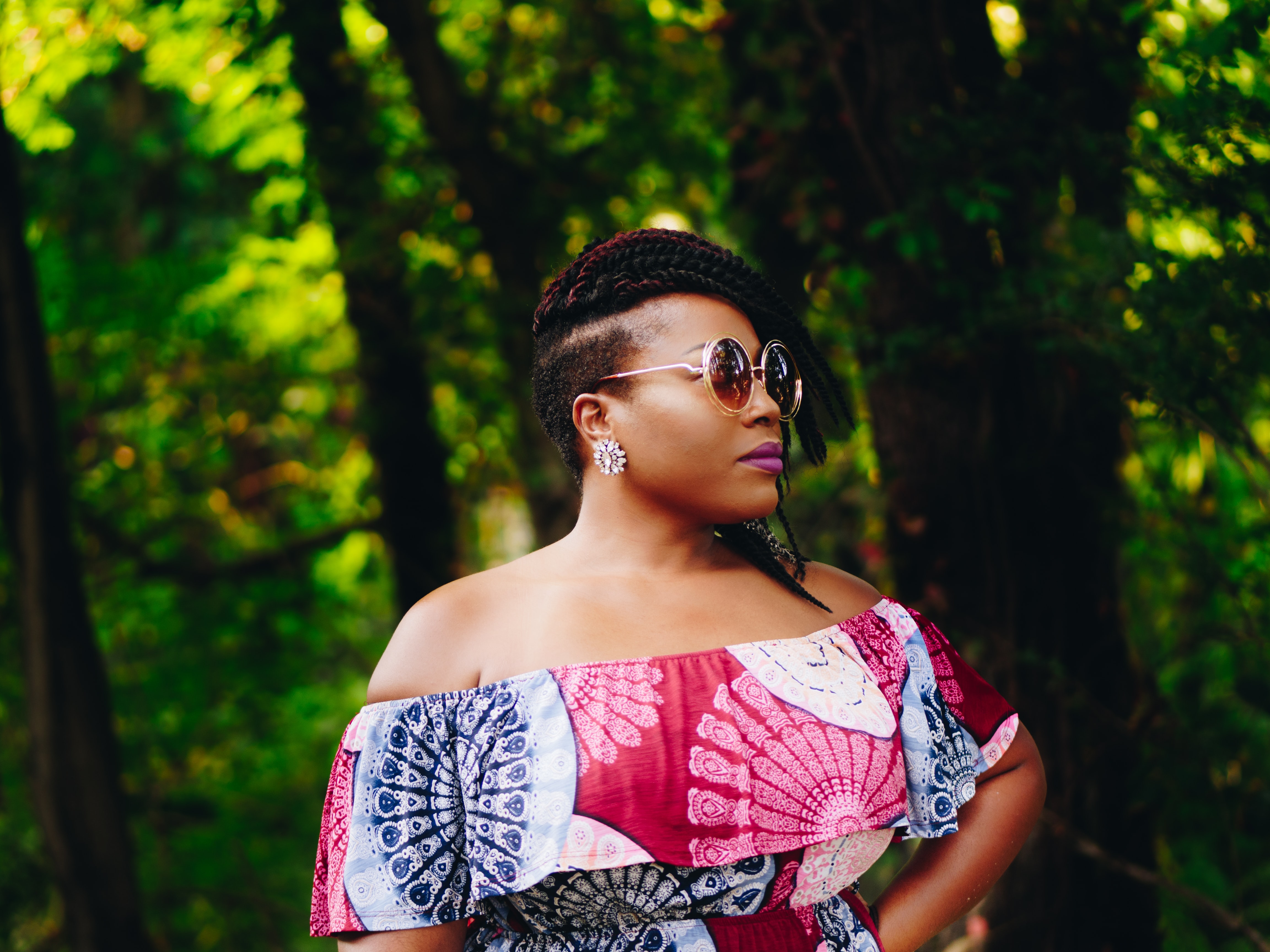 Confident black woman wearing a colorful top and sunglasses against a forested background