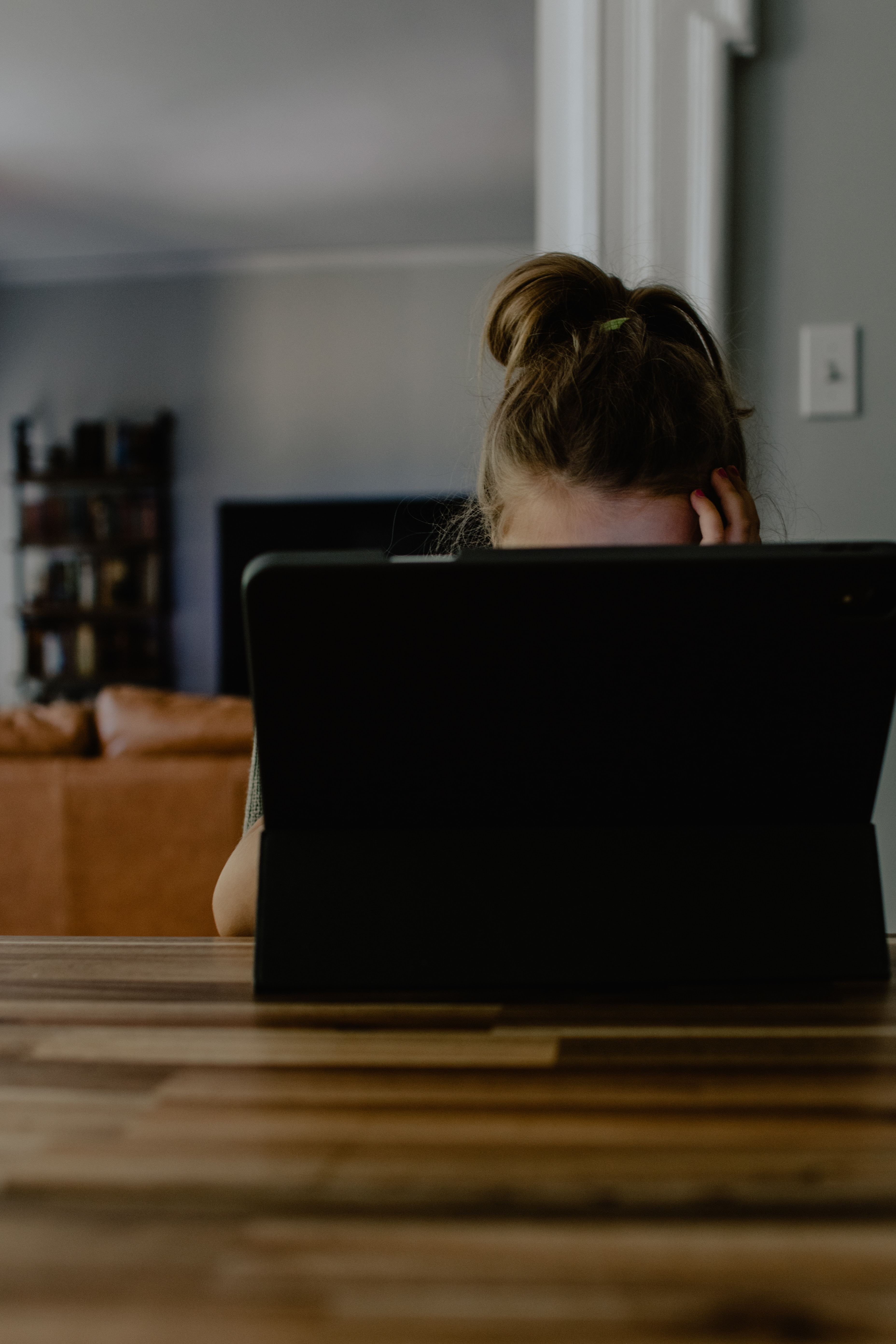 Womans forehead can be seen over the top of a laptop. From the position of her hand on her face, you can tell she is frustrated.