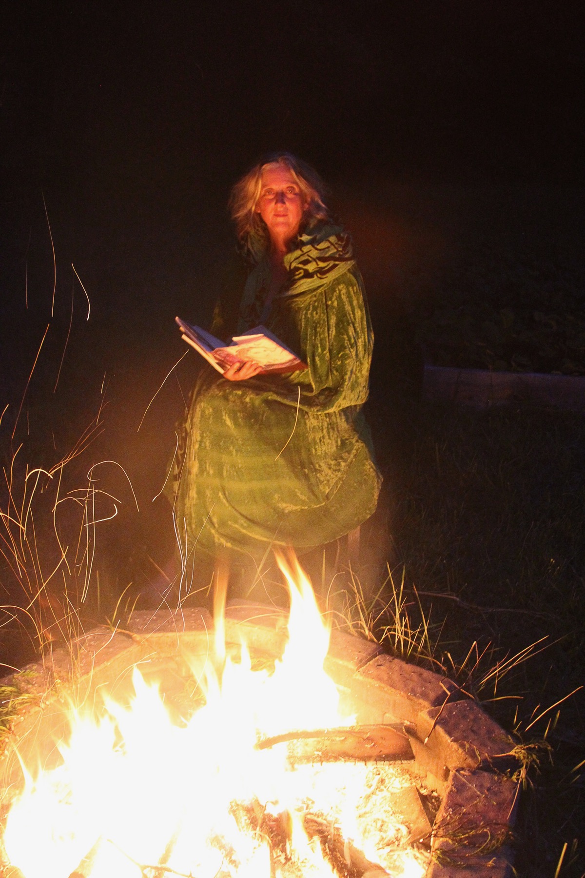 Photo of woman before a fire in a green cloak