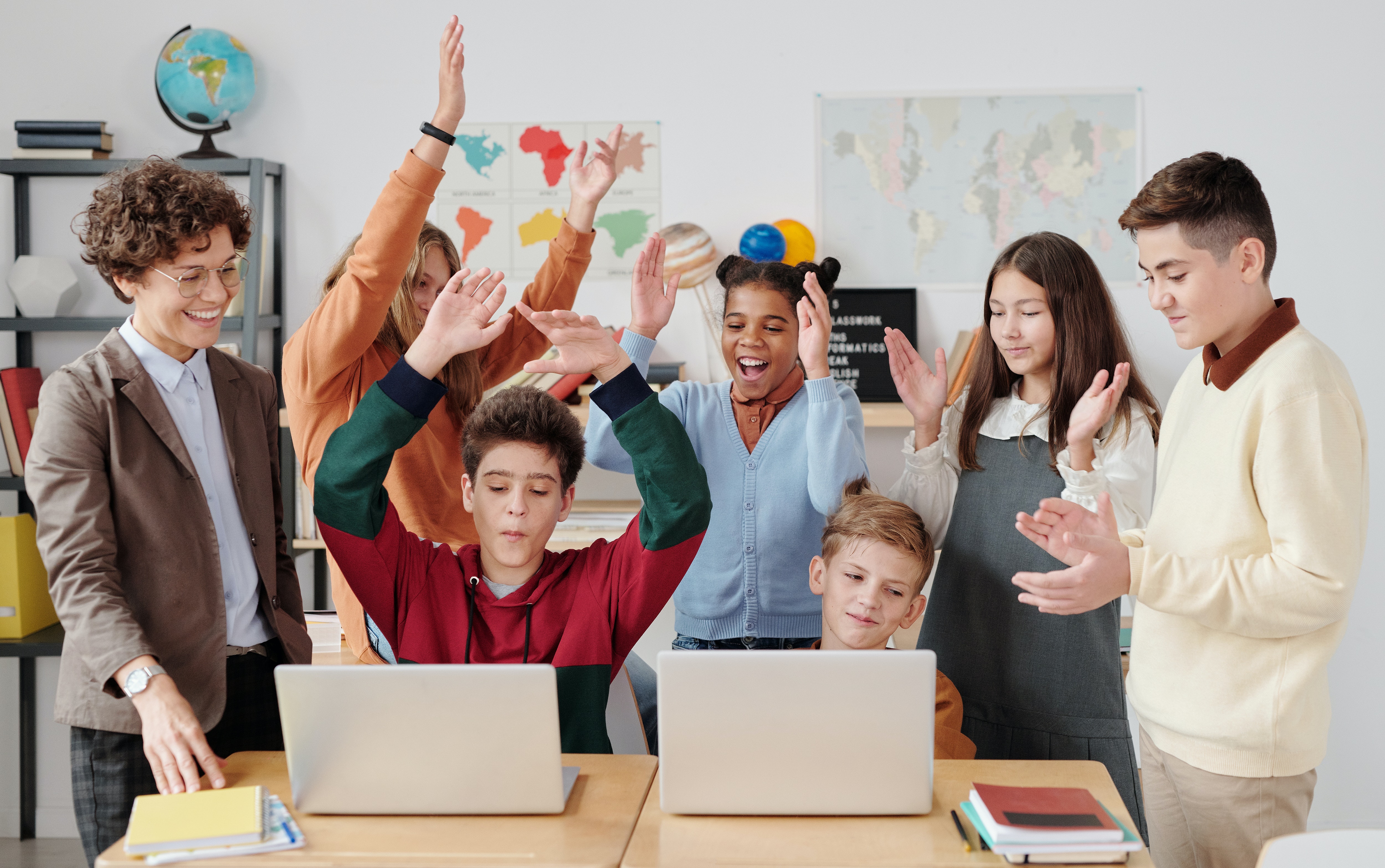 students in front of laptop cheering with hands raised