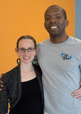 Kate Feinberg Robins and DeShawn Jamar Grim Robins, an interracial couple in their 30s, smiling with arms wrapped around each other in front of an orange wall