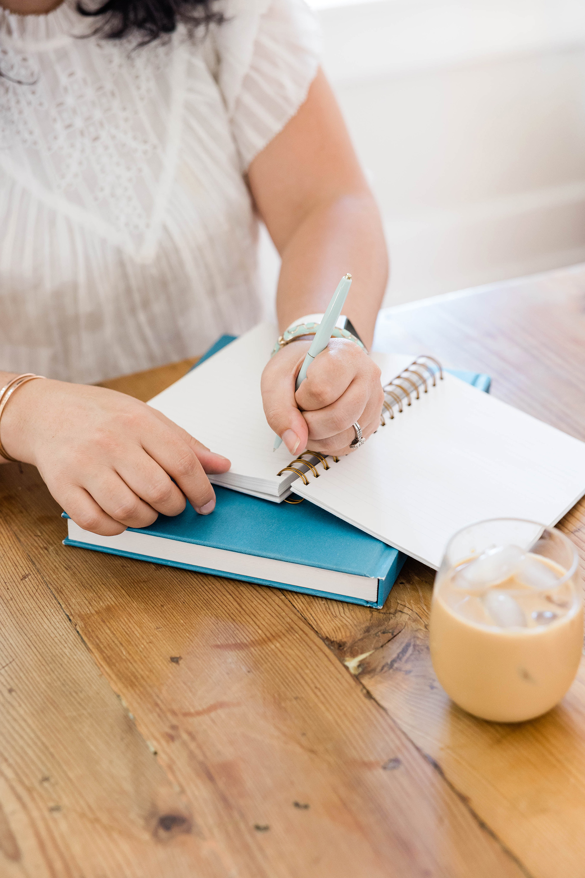 Woman writing in a notebook with a glass of iced coffee.