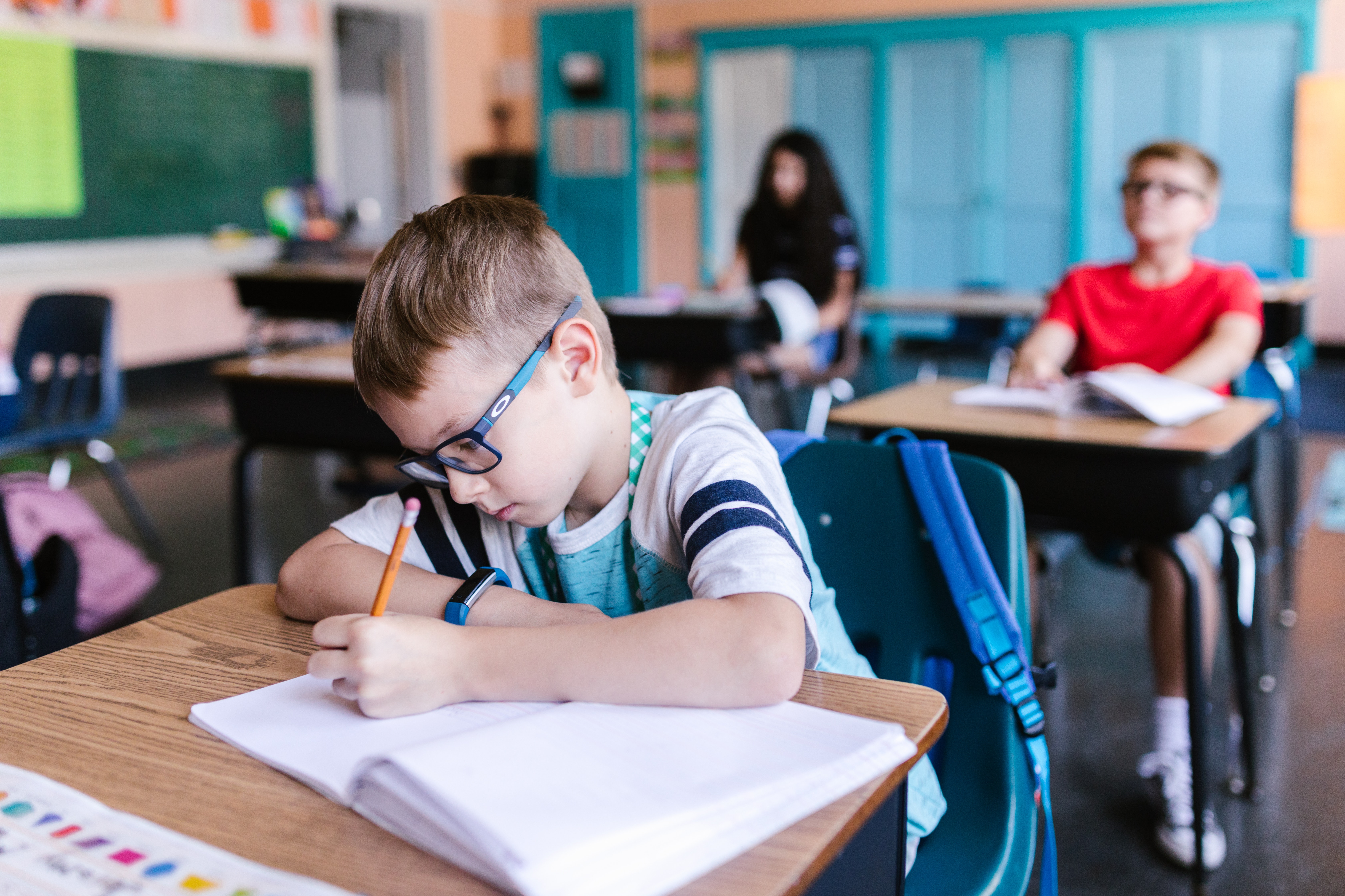 boy in classroom writing out a math equation in his notebook