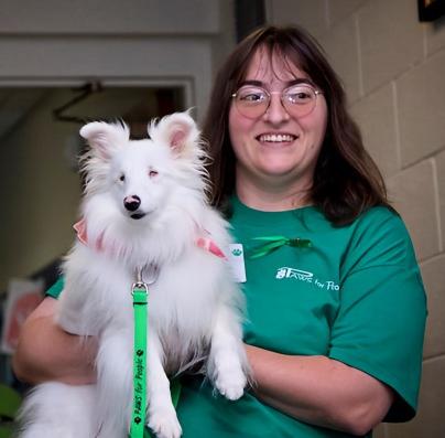 Deb carries a small white fluffy blind and deaf dog in her arms.
