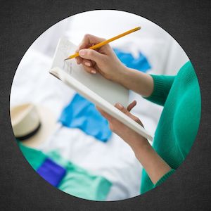 woman writing in notebook next to clothes on bed