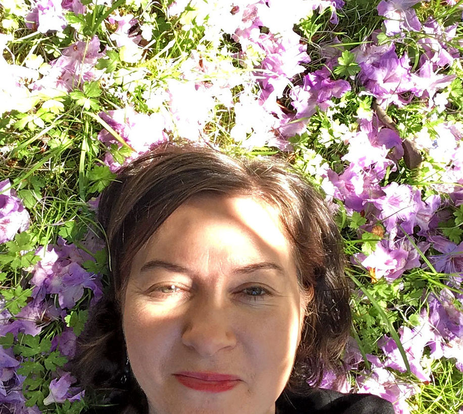 A woman with brown hair laying on top of a ground with purple flowers.