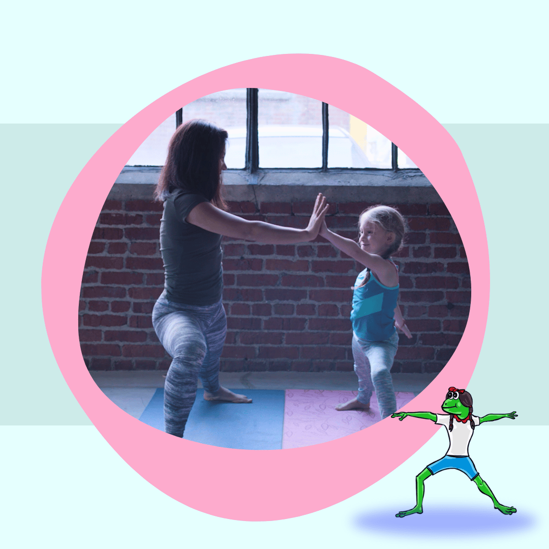 A teacher and young student stand facing each other. Legs are in a high lunge position and they reach across their yoga mats to touch hands in a high five.