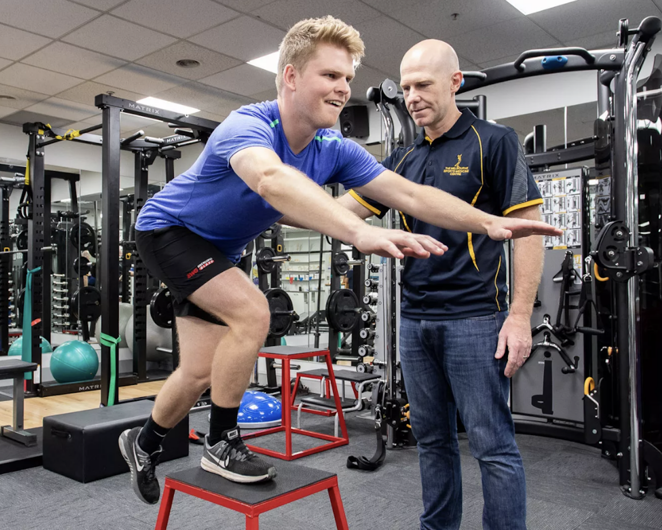 Mick Hughes supervising client with ACL post-reconstruction rehab, doing leg raises exercises on stool.