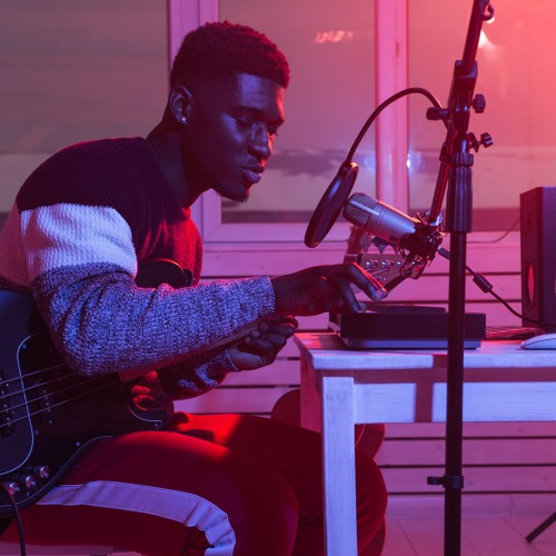 Man seated in a project studio facing a microphone and playing a keyboard controller