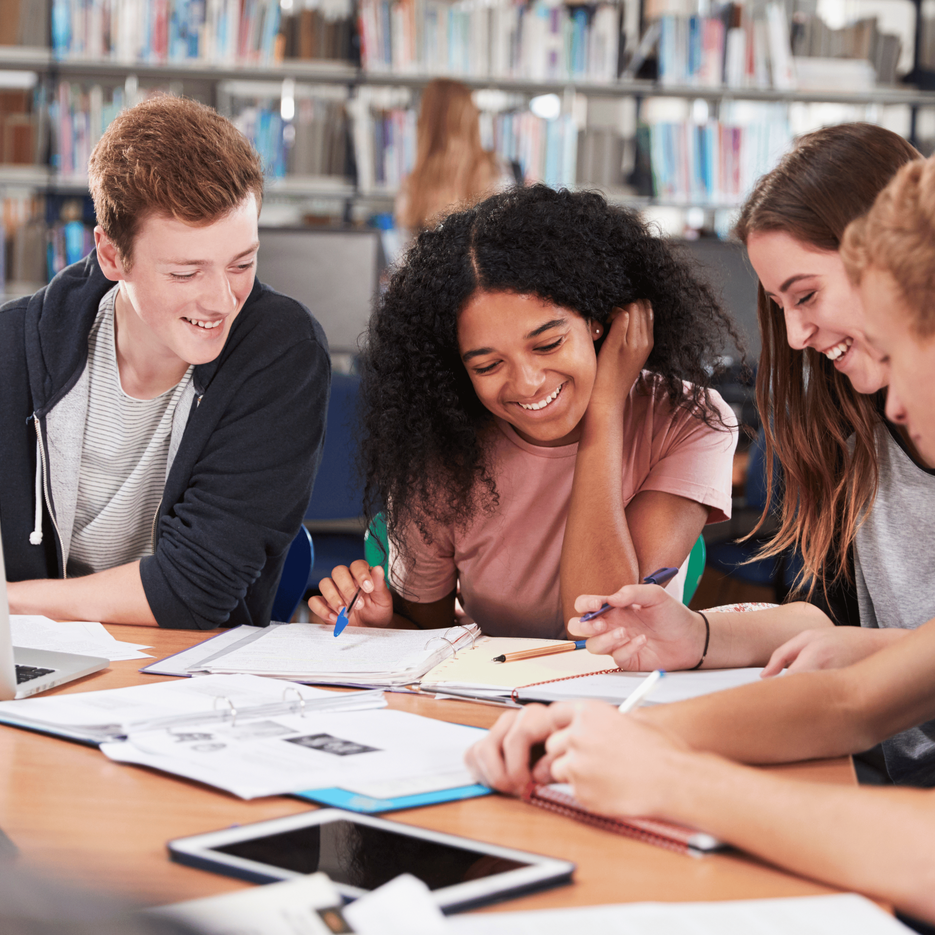 four students sitting at a table looking over notebooks and smiling