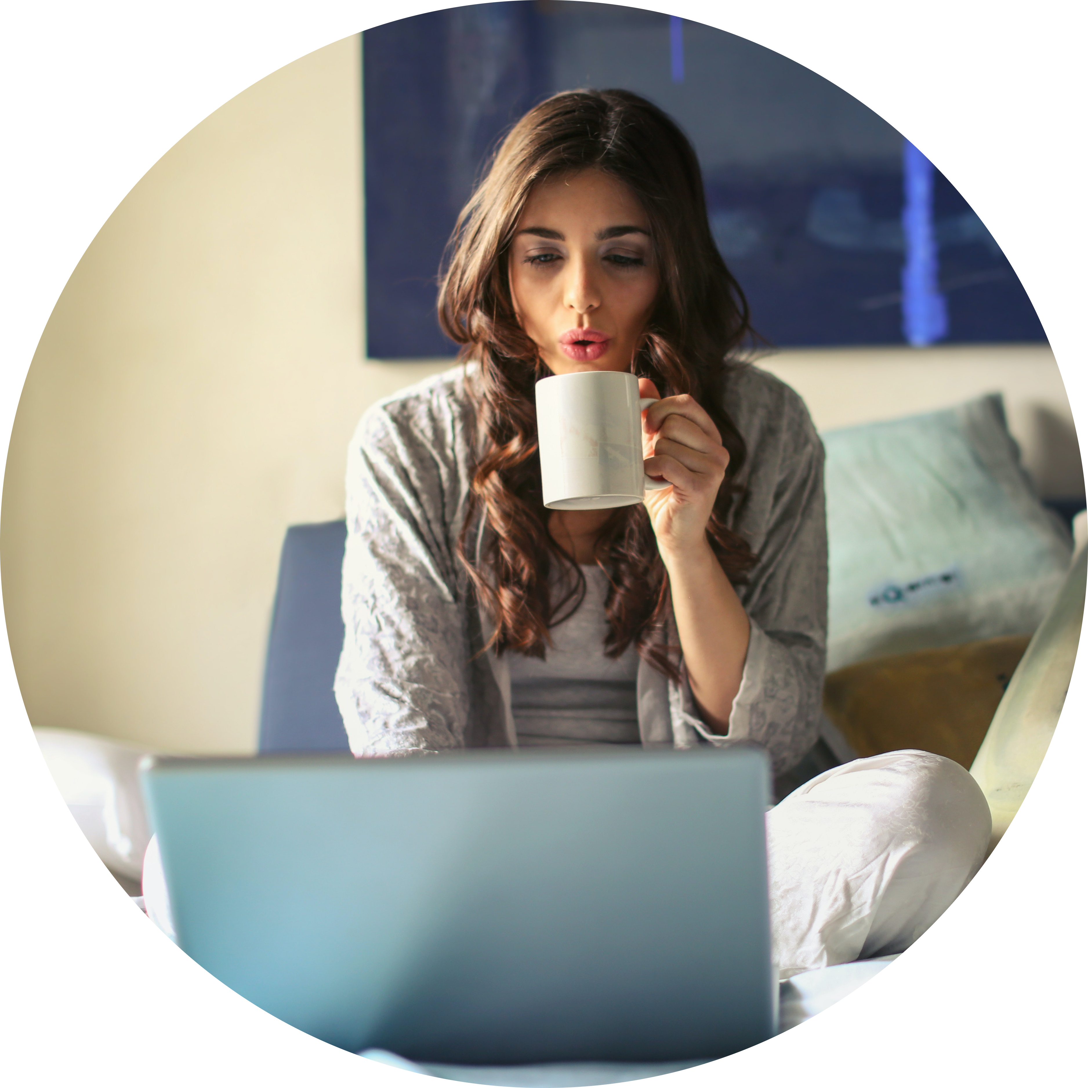 A woman sitting on her bed, drinking a cup of coffee, while she reads Psycophi's blog about self-care habits and mental health education.