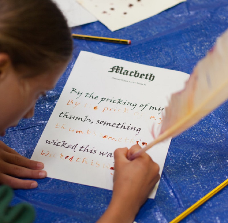 A young girl is practising writing with a quill