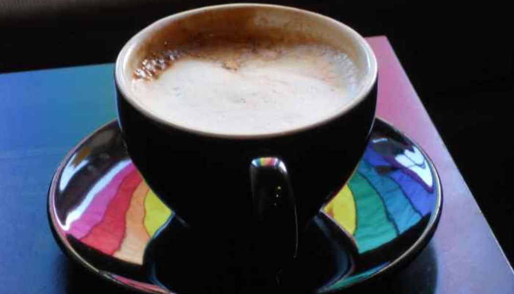 The reflection of a rainbow flag in a black espresso mug and saucer. 