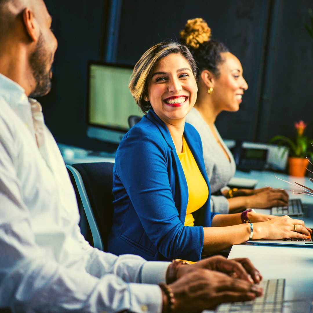 Three people sitting at computers smiling at each other