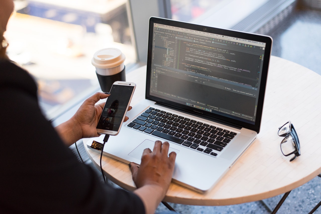 Black woman reviewing lesson on phone while coding on computer