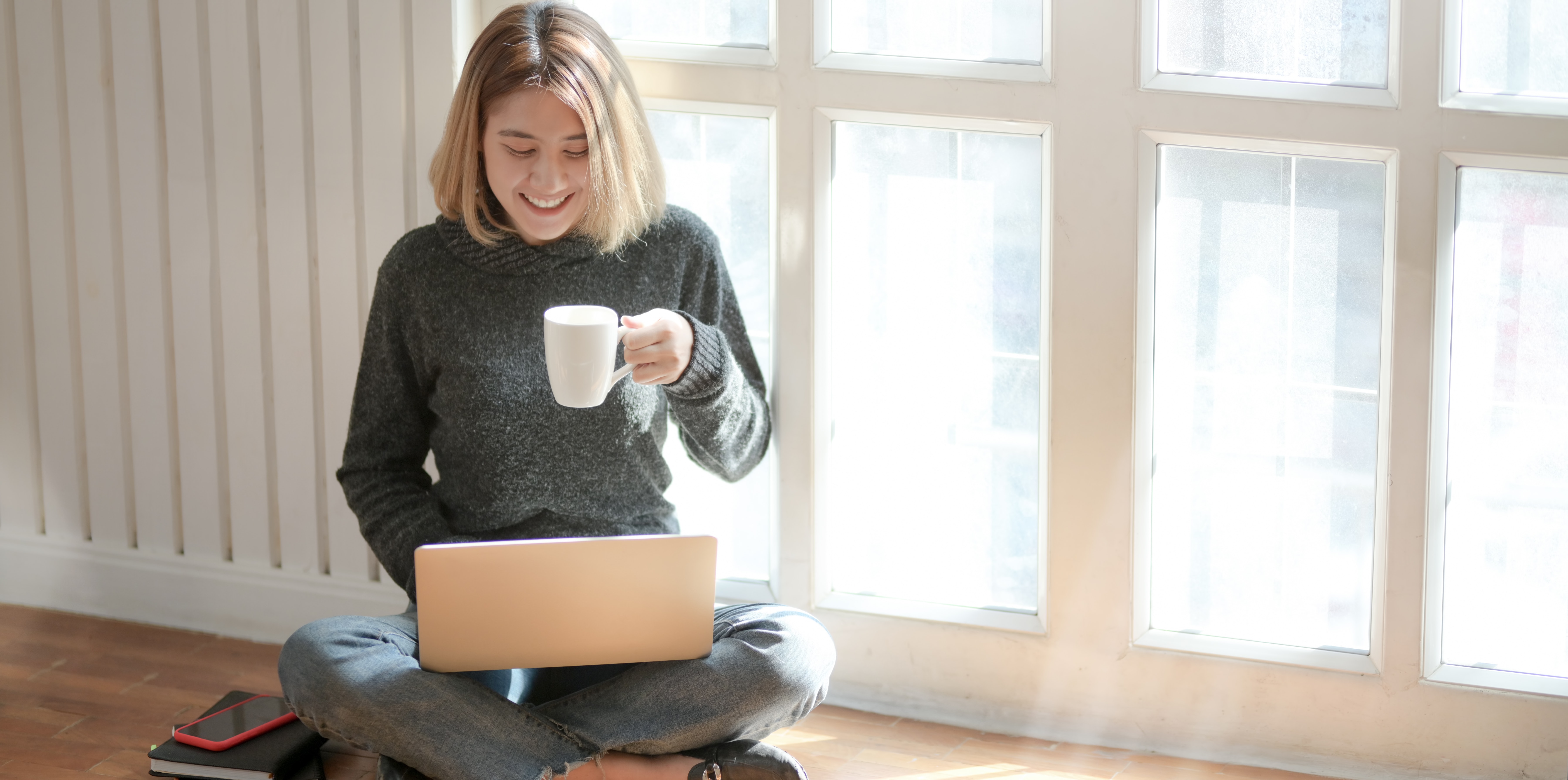 Asian woman drinking coffee and using her computer on the floor