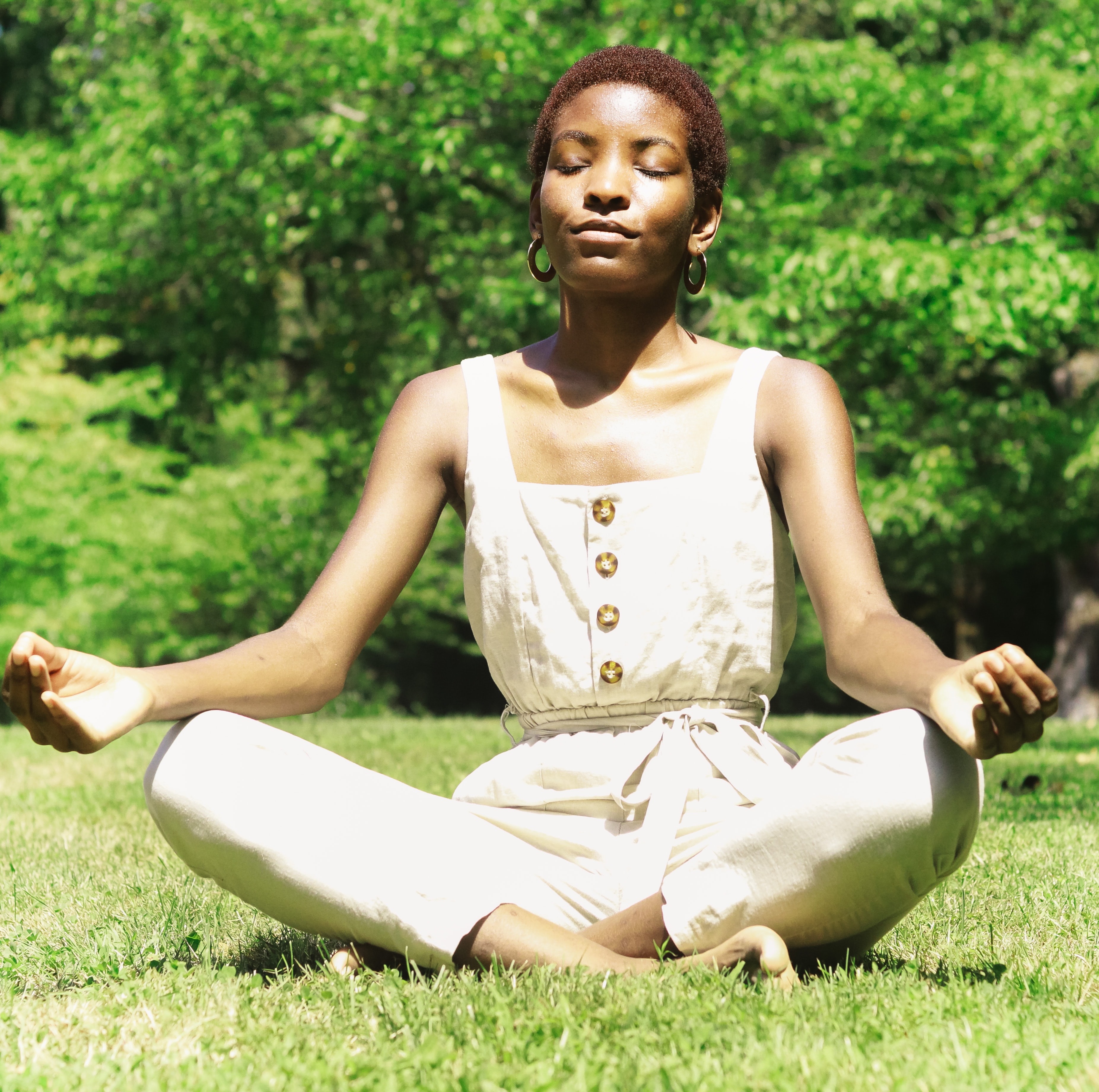 Black woman sitting on grass meditating with green trees in background