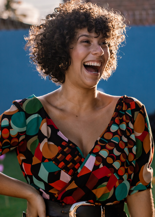 smiling, confident woman wearing brightly colored, beautiful blouse and stylish belt