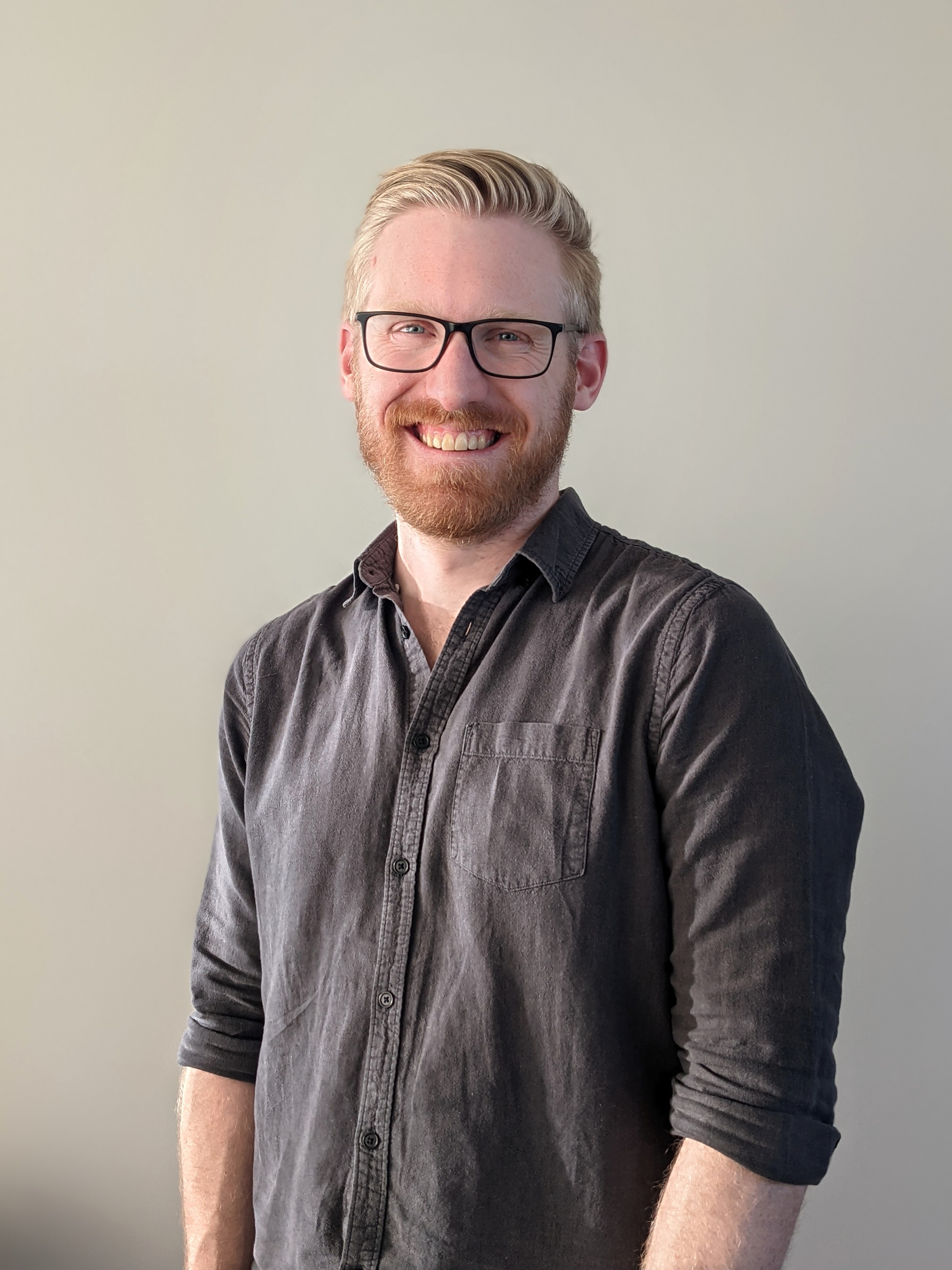 Andrew smiling, wearing black-rimmed glasses and rocking a sleek, swooping hairstyle.