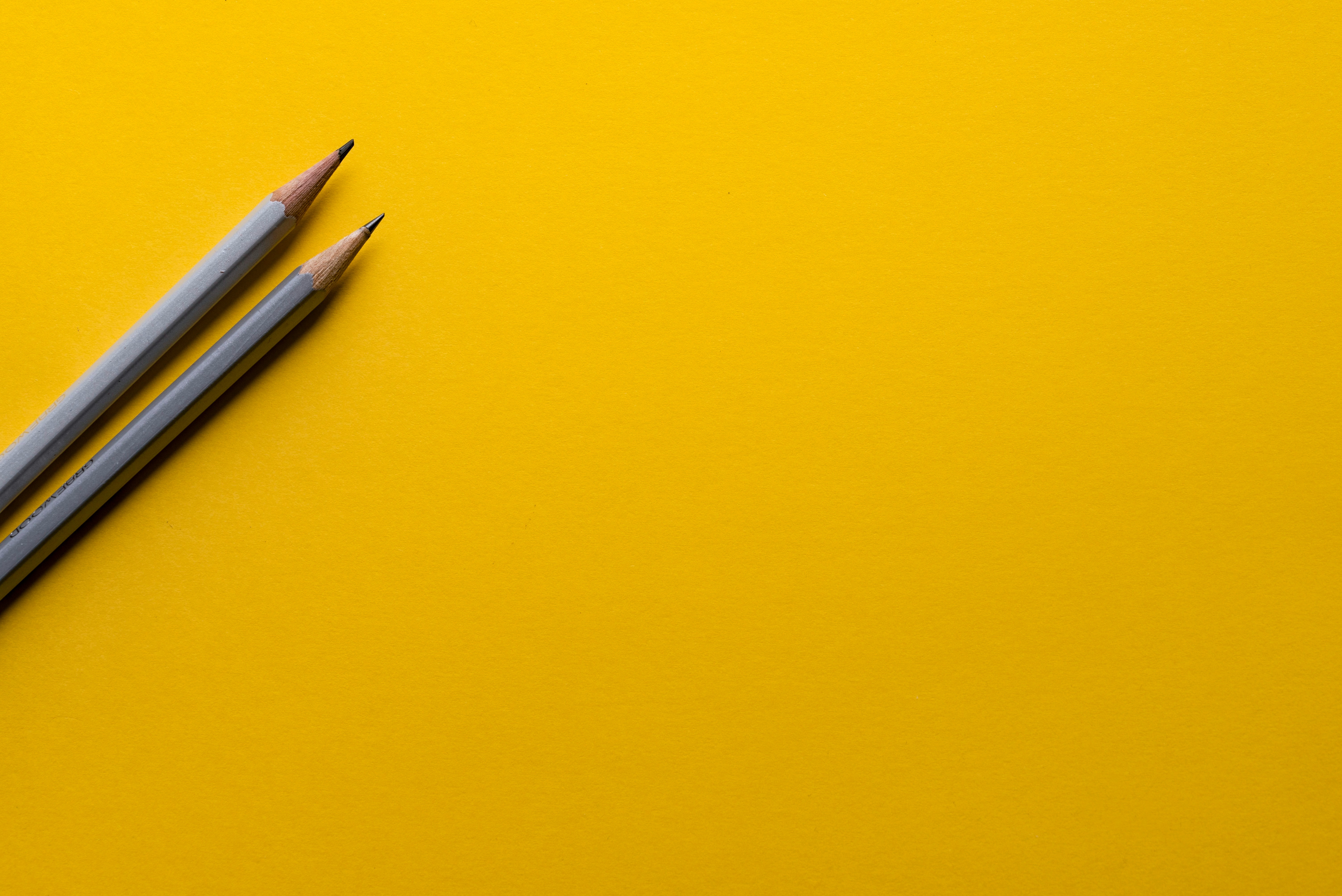 Image of two sharpened, gray pencils laid on an orange piece of paper