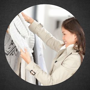 young woman smiling at sweater she is holding up in front of shopping rack of clothes