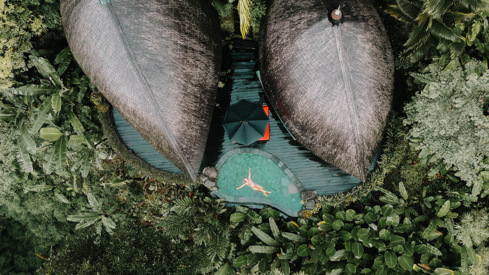 girl floating in pool by two huts in a jungle in Bali