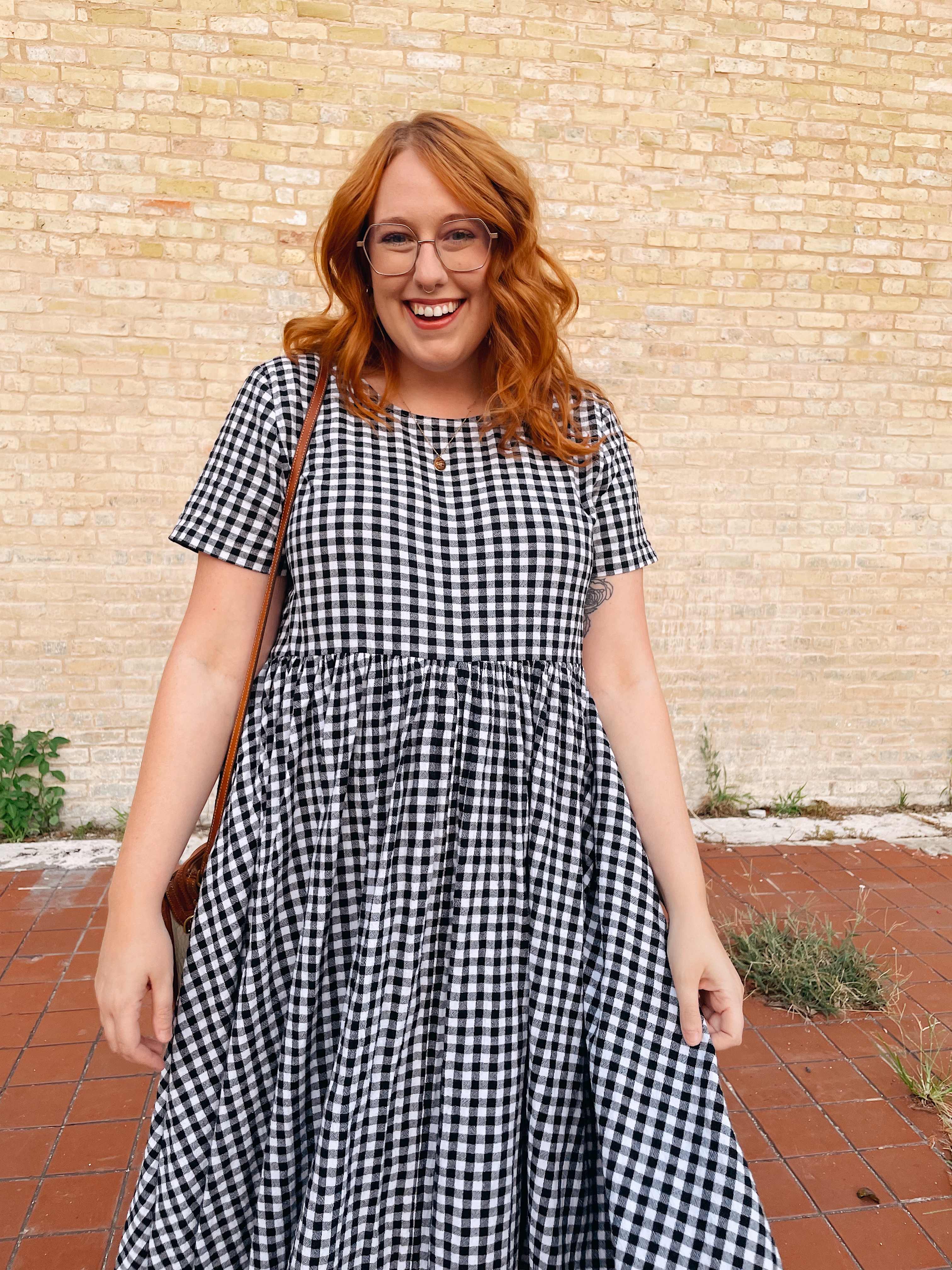 Nic standing in front of a brick wall with curled ginger hair and a gingham dress