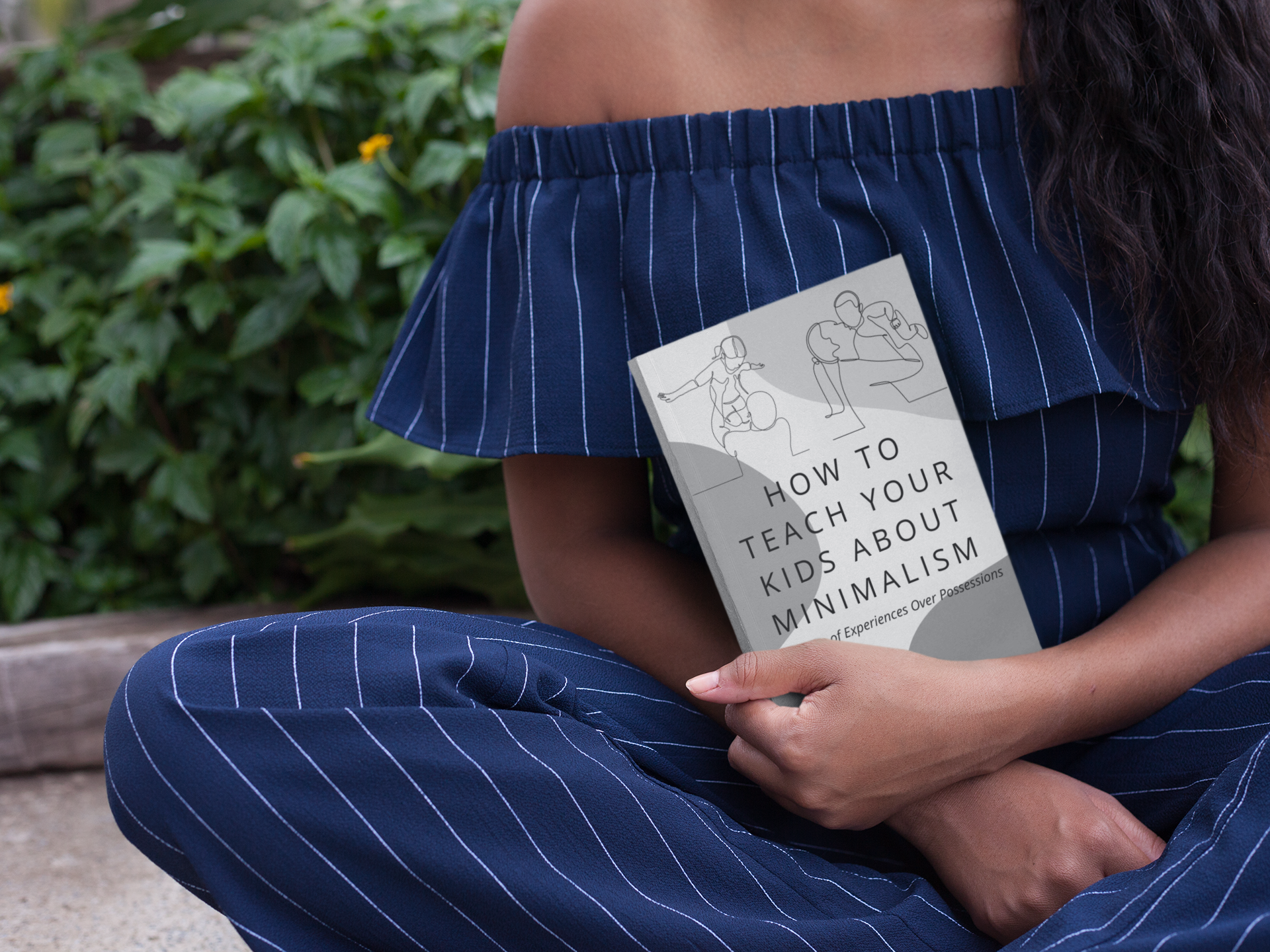 black woman sitting with her legs crossed holding a book titled, How to Teach Your Kids About Minimalism