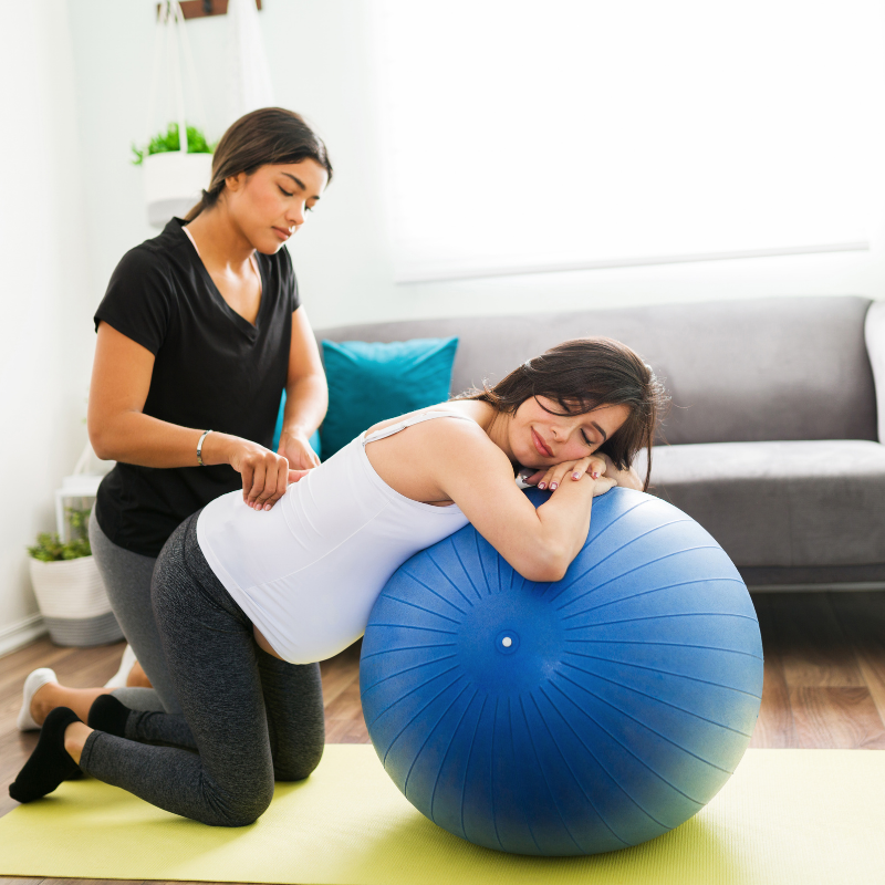 woman leaning over birth ball with partner behind rubbing back