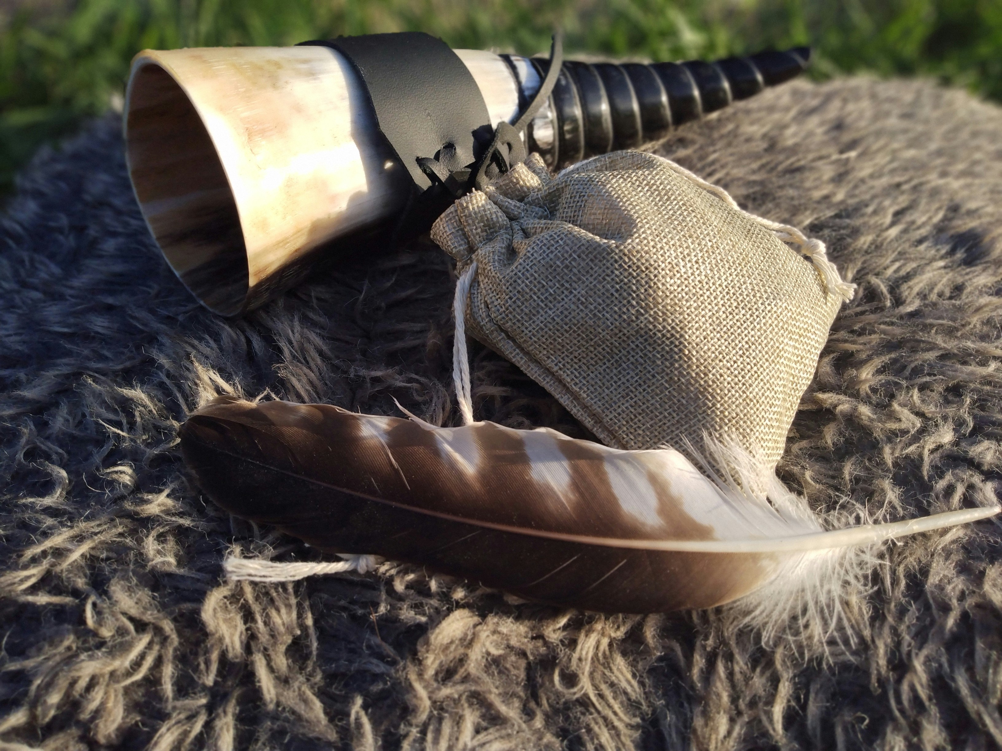 a set of runes in a bag, with a feather and a drinking horn, resting on top of a sheepskin