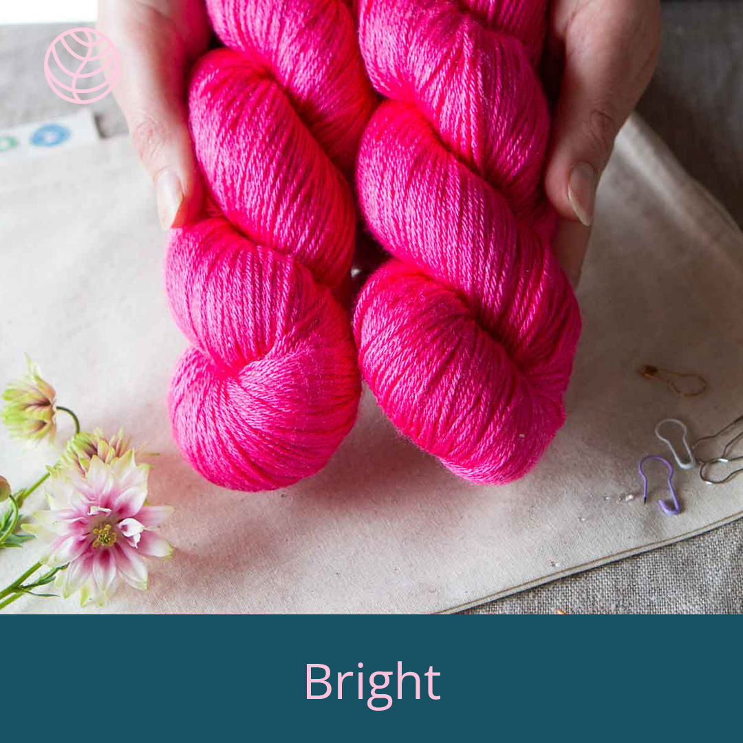 Hands holding two skeins of vibrant pink yarn.