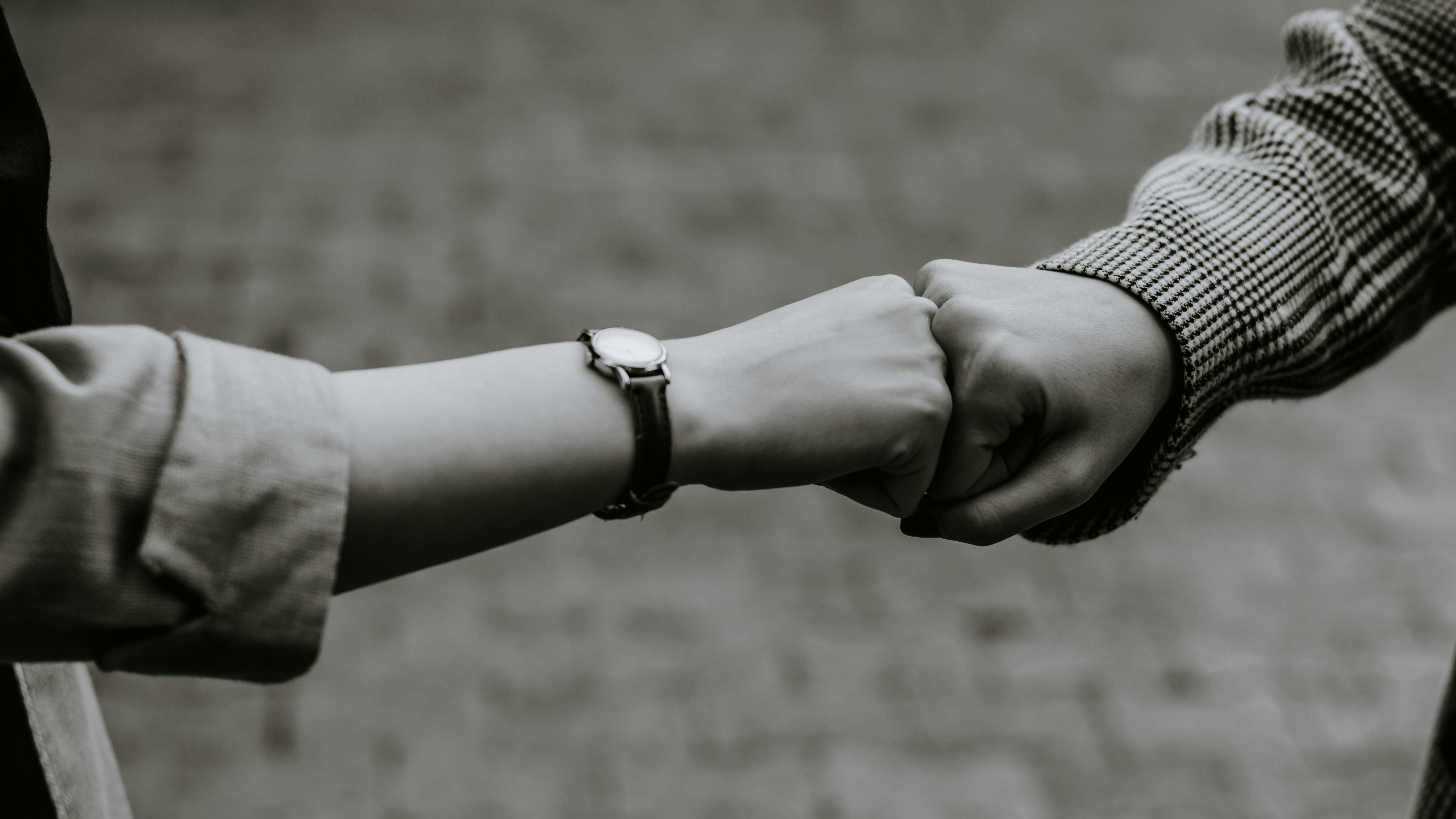 2 people affirming they can do it with a shared fist bump, one arm has a watch and folded cuff, the other has a plaid sleeve that disappears off the edge. Image is black and white