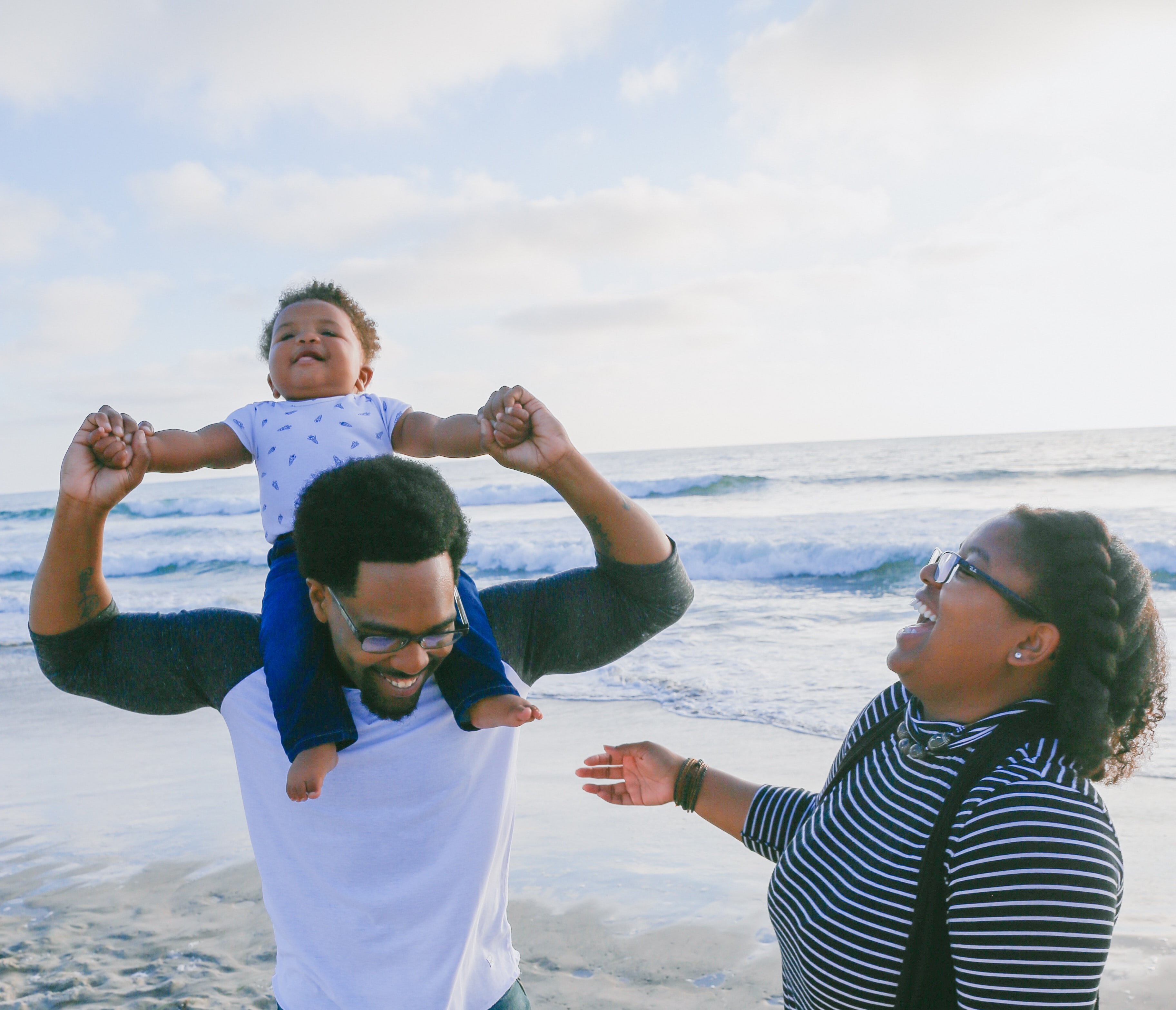 Black family joyfully on the beach while waves gently crash behind them