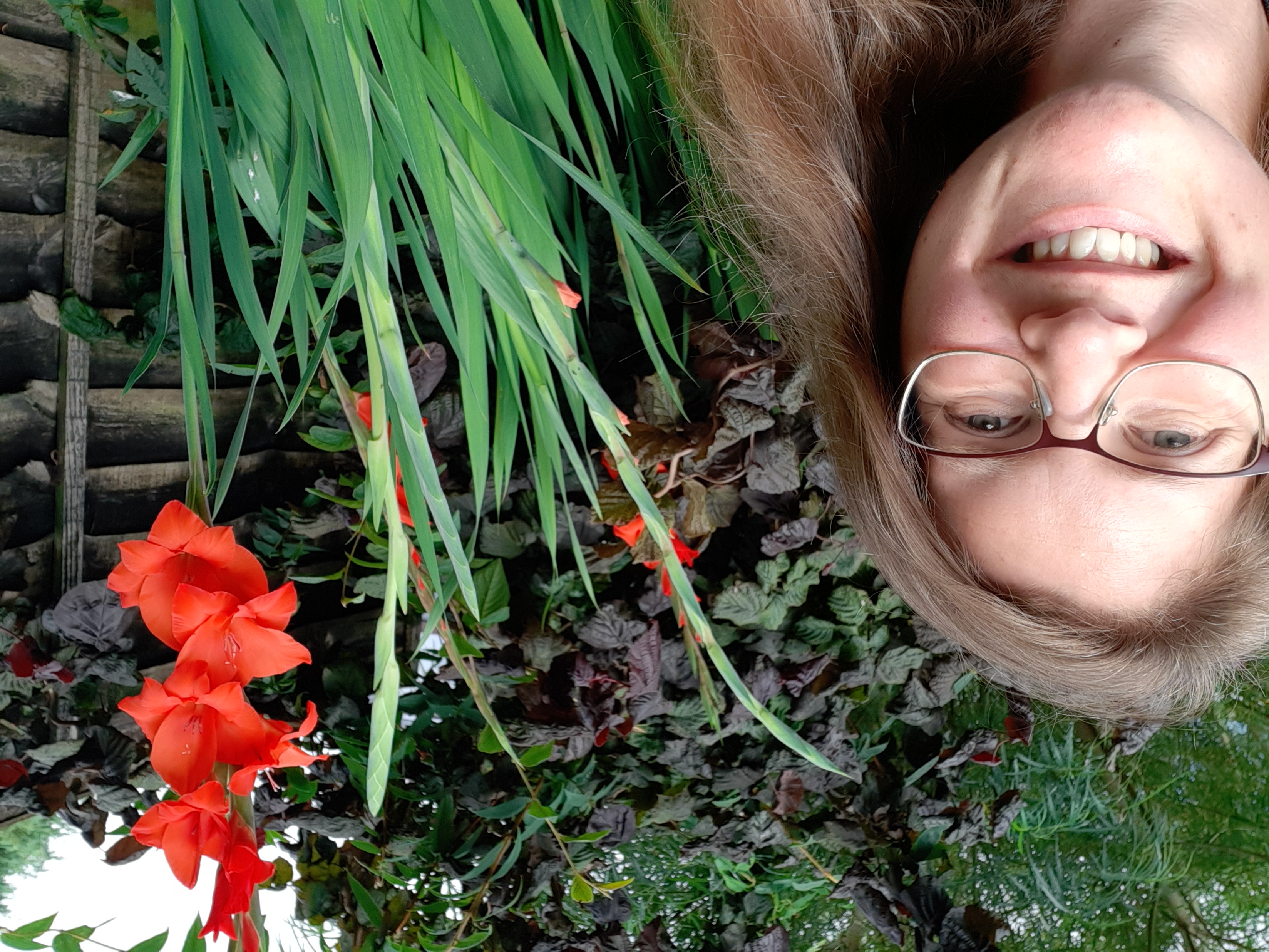 A photo of me smiling in my garden, next to some beautiful red flowers