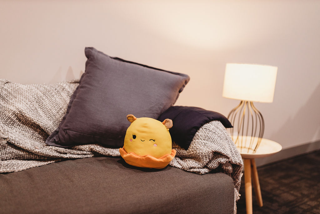 A couch with a yellow squish mellow, pillow blanket and soft lamp light.