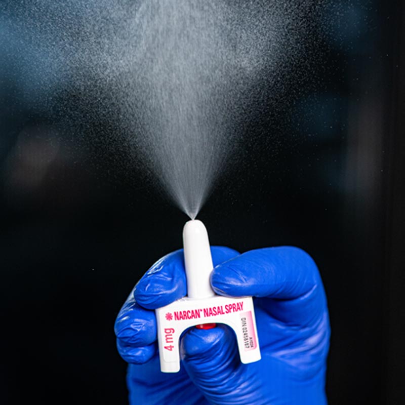 A person wearing blue gloves is pressing a naloxone spray as a demonstration. 