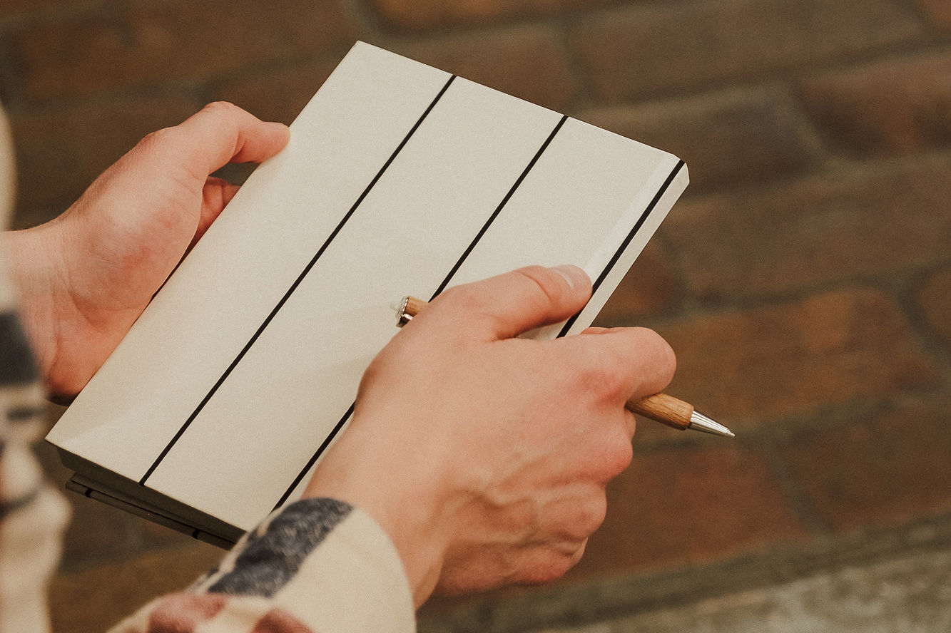 Jemand hält ein weiß-schwarz-gestreiftes Notizbuch und einen Kugelschreiber in der Hand