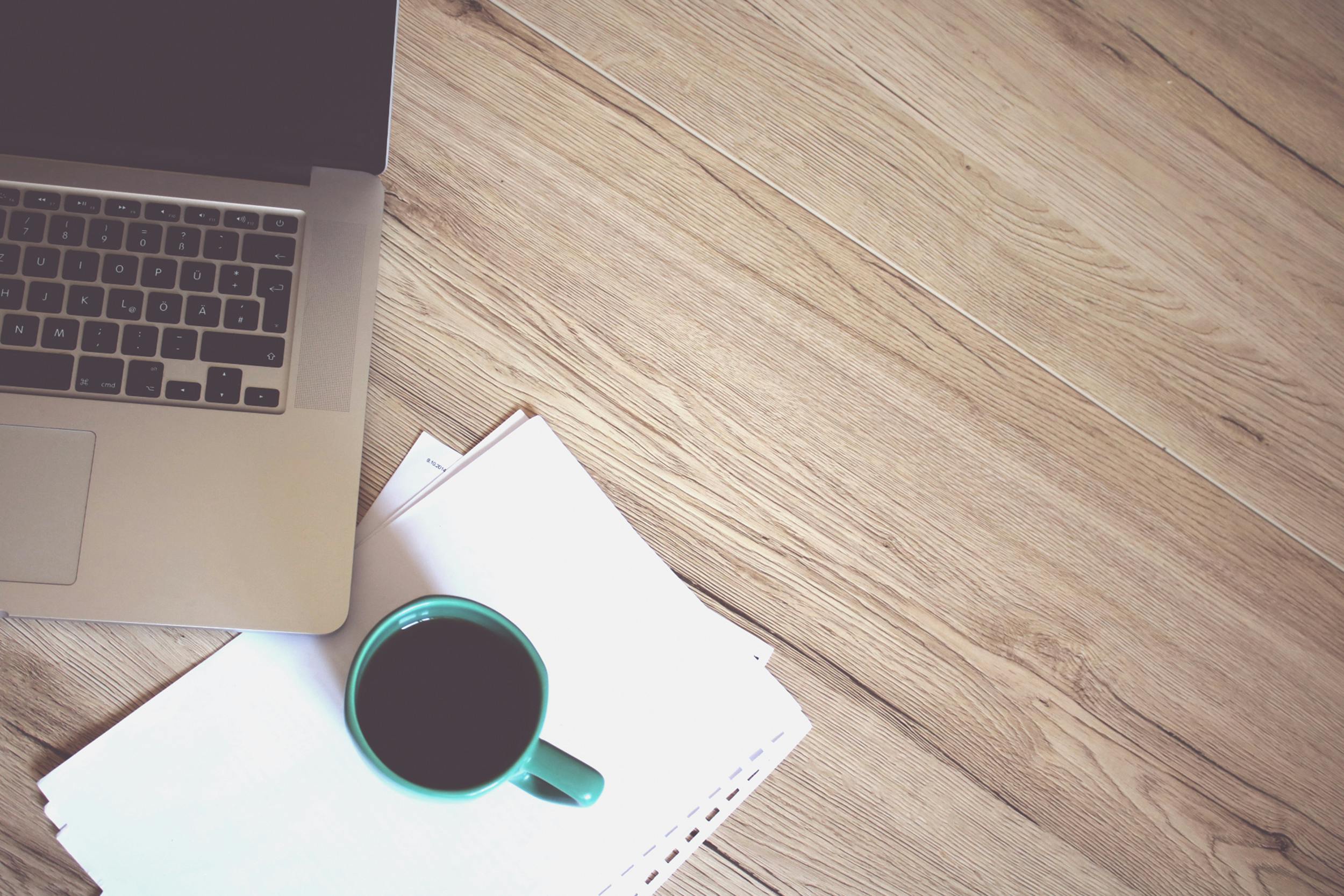 A wooden desk with a laptop and coffee cup setup for online learning.