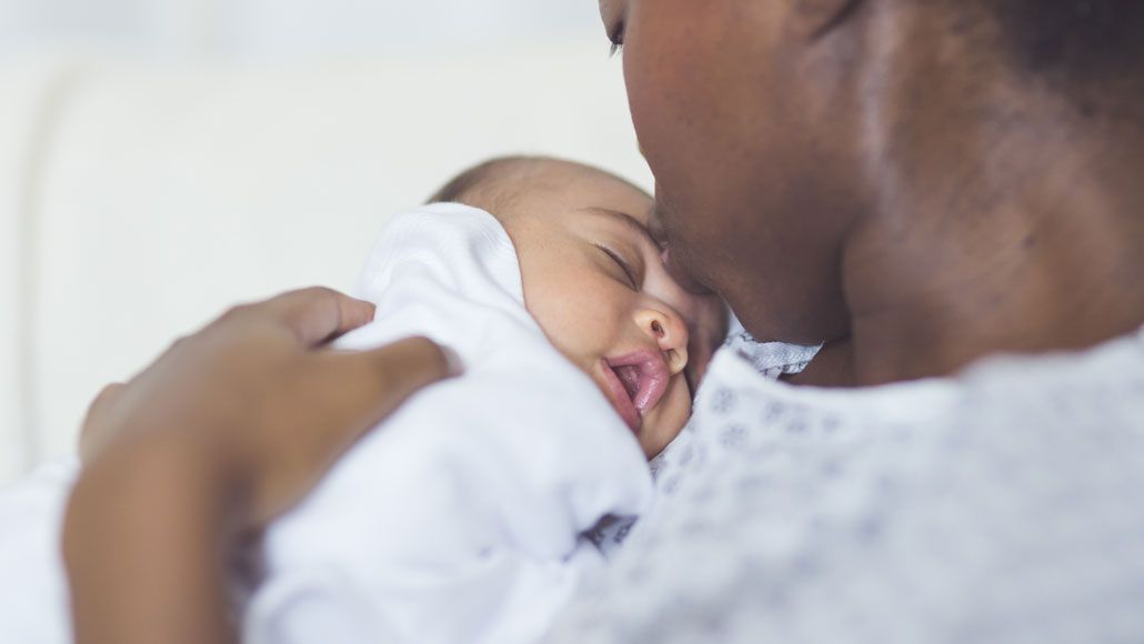 Black mother in a hospital gown holding a Blak newborn baby adn almost about to kiss him. 