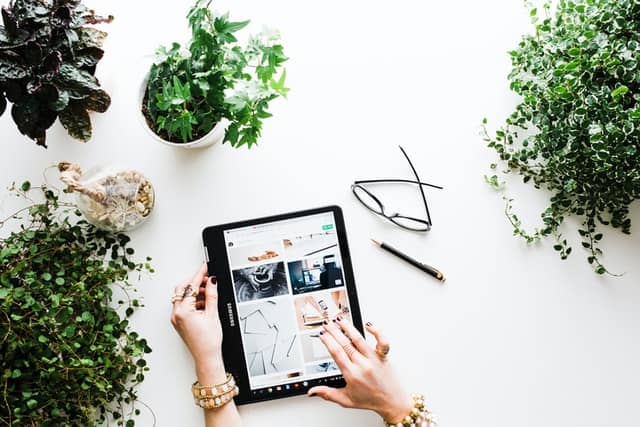 Photo credit and description: Brooke Larke from Unsplash. The photo shows a tablet surrounded by green plants, glasses, and a writing tool. 
