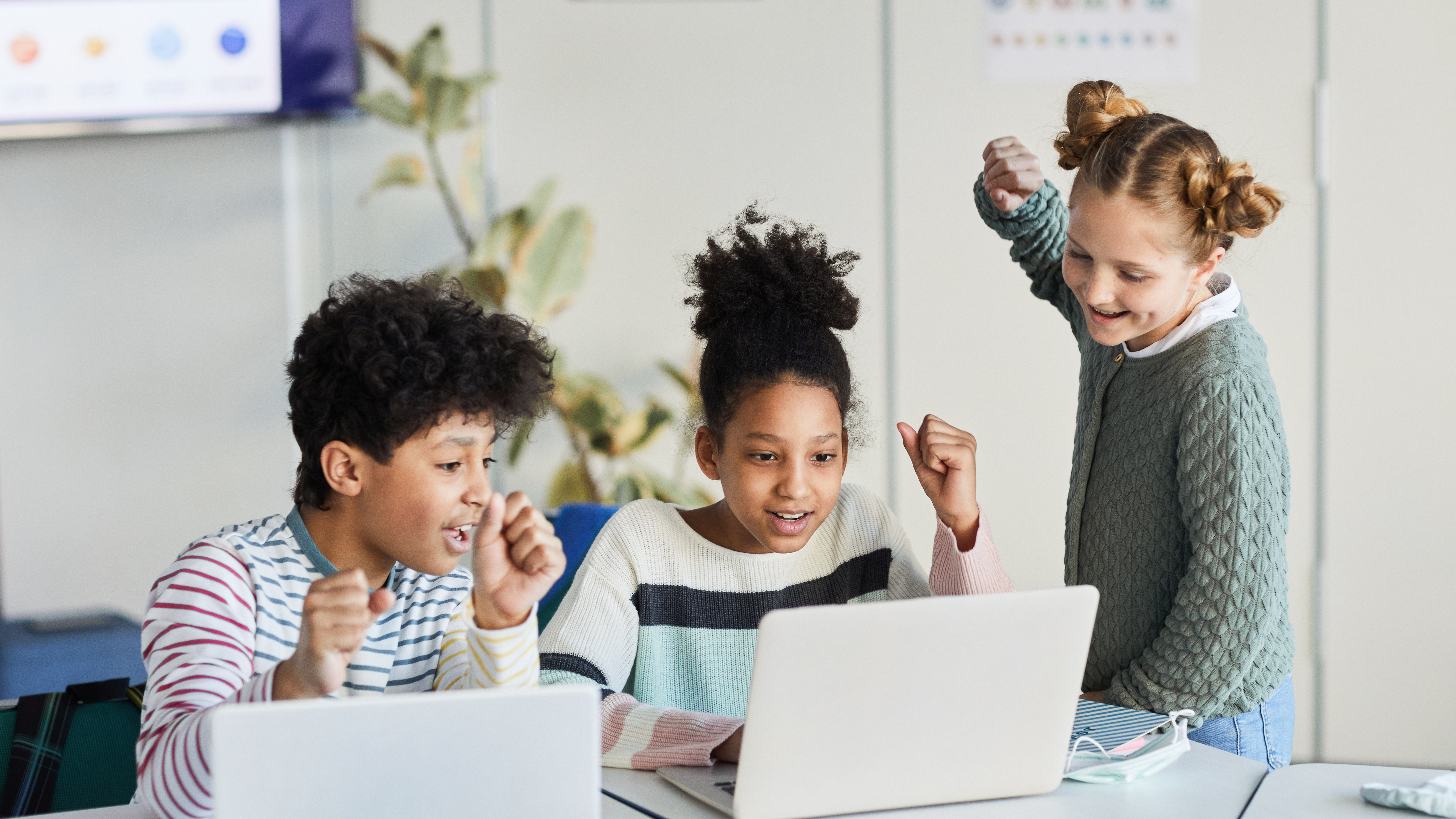 three students cheering in front of laptops