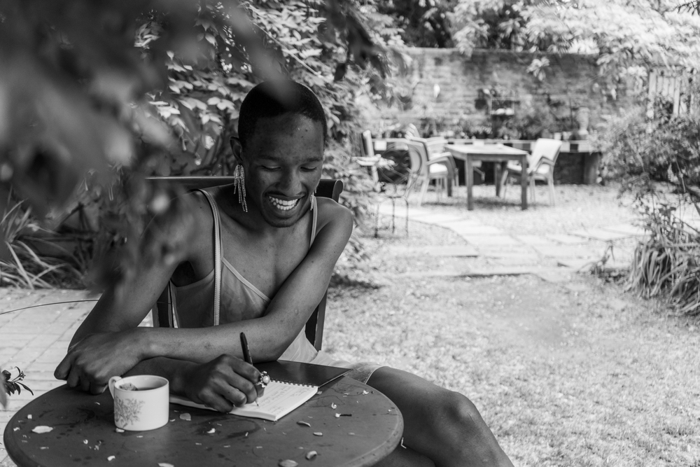 A queer black male enjoys a deeply intimate moment while journaling outdoors on a day dedicated to self-love.