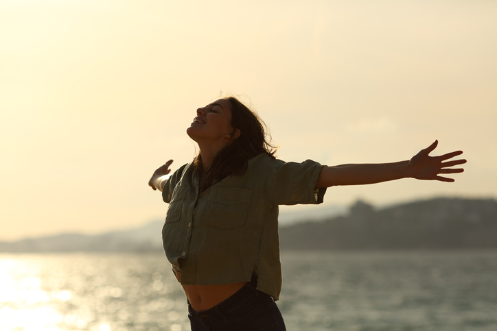 Female standing in front of water with arms stretched out to the sides